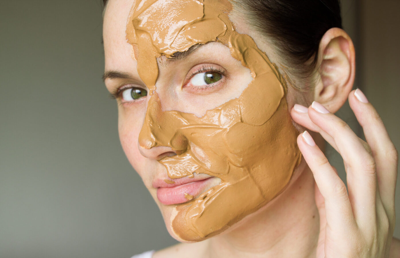 Woman applying vegan red clay face mask to half of her face